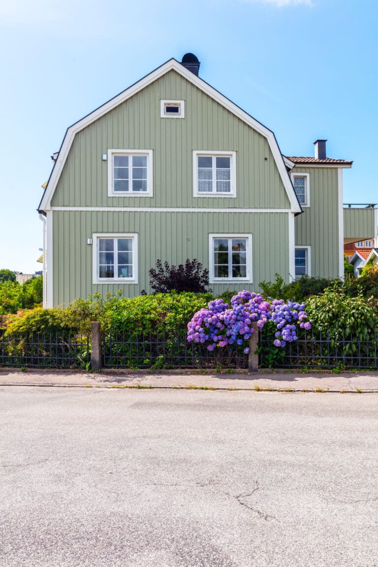 Grönmålad träfasad på tvåplansvilla med vita foder och blommor i framkant