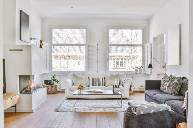 Ljust vardagsrum med öppna fönster, soffor och modern eldstad