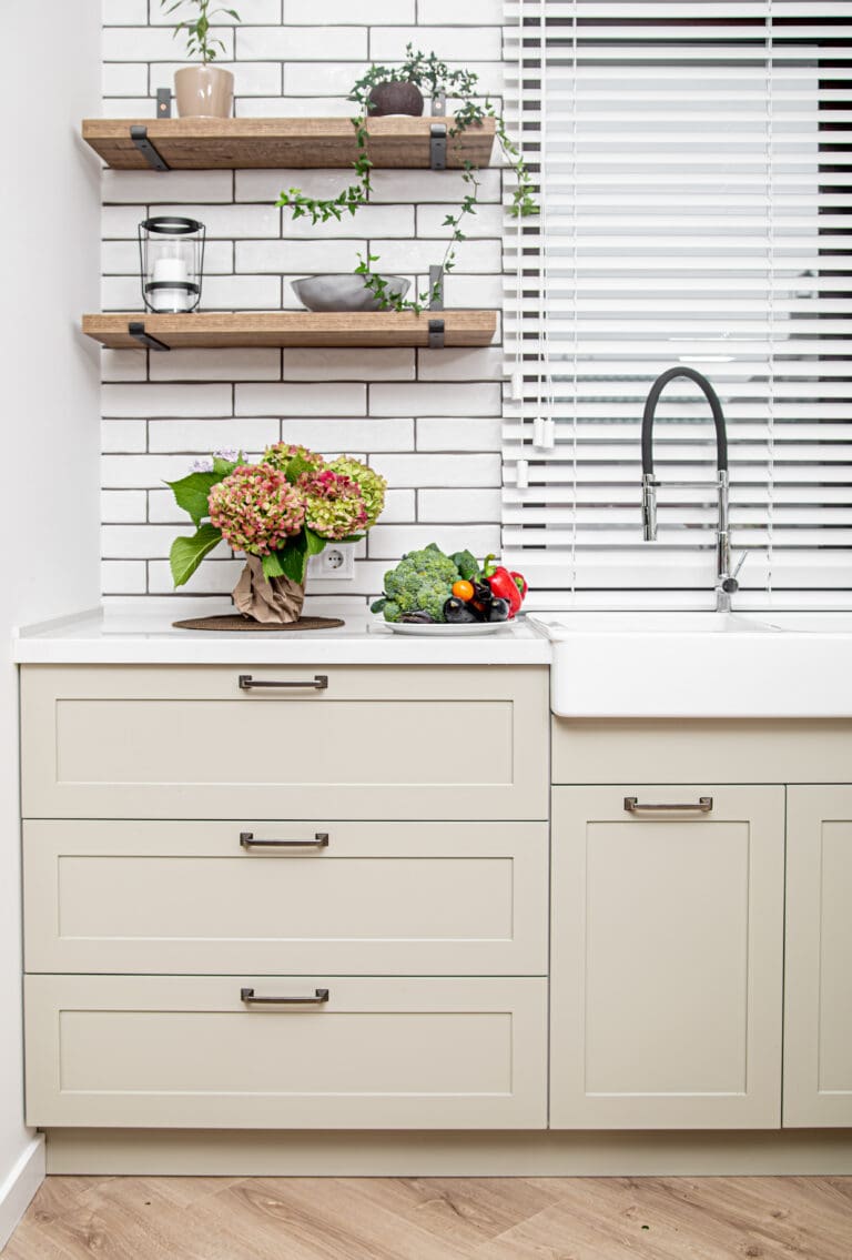 Modern köksbänk med beige luckor, vit kakelvägg och öppna trähyllor
